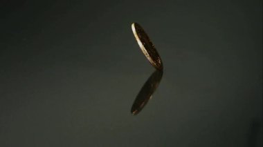 Antika bir özgürlük, karanlık bir yansıtıcı yüzey üzerinde hızla dönen beş dolarlık altın paranın başı sonunda yavaşlayana ve tamamen durana kadar.