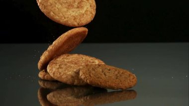 Koyu bir yansıtıcı yüzeyin üzerine tek tek düşen altın kahverengi tarçınlı kurabiyeler katı siyah bir arkaplana karşı lezzetli bir yığın oluşturuyor.