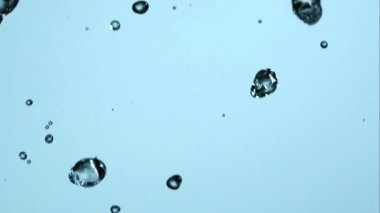 Kristal berrak su damlacıkları ve sıvı, parlak mavi bir zemin üzerinde yüksek hızlı çekimde dans ederek saf su ve tazeliği vurguluyor.