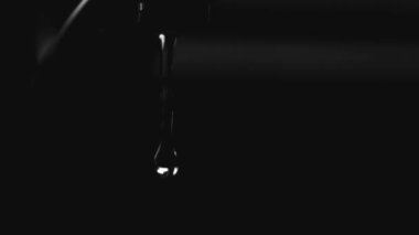 Su damlacıklarının, karanlığa karşı yüksek kontrastlı siyah-beyaz bir musluktan sürekli bir akış haline gelmesinin detaylı yavaş çekim görüntüleri.