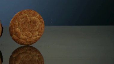 Yulaf ezmesi ve çikolata parçalı kurabiyeler gri yansıtıcı yüzeyde koyu mavi arka plana karşı ağır çekimde ağır çekimde yuvarlanıyor.