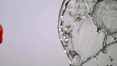 Üç taze olgun kırmızı çilek düşüyor ve havada uçuyor büyük kristal berrak bir suyla çarpışmak için beyaz bir zemine çarpıyor.