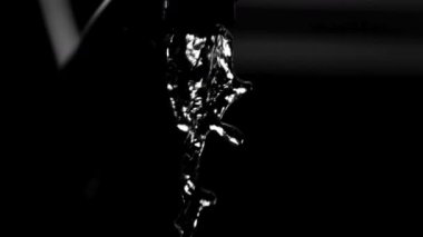 Dar bir kristal berrak su akıntısı, derin siyah bir zemine dikey olarak düşüyor. Detaylı damlacıklar ve sıvı dalgalanmaları yavaş çekimde yüksek kontrastlı ışıklandırmada gösteriyor.