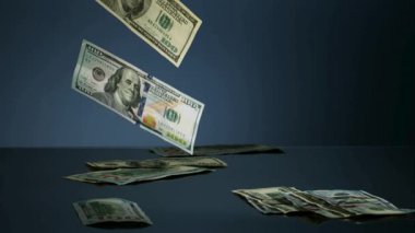 Birçok yüz dolarlık banknotlar yukarıdan düşüyor ve yavaş çekimde finansal kazancı ve zenginliği gösteren koyu mavi yansıtıcı bir yüzeye iniyor.