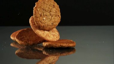 Yulaf ezmesi ve tarçınlı kurabiye gibi farklı yuvarlak kurabiyeler yavaş çekimde siyah yansıtıcı bir yüzeye düşüp zıplıyorlar.