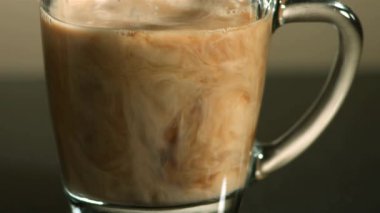 Taze süt ya da kremanın şeffaf bir bardak sıcak siyah kahveye karıştırılıp yavaş çekimde güzel girdap şekilleri oluşturulduğu aşırı yakın çekim görüntüsü.