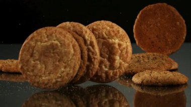 Birbiri ardına düşen yuvarlak çerezler koyu bir arka plana karşı siyah yansıtıcı bir ayna yüzeyinde üst üste yığılıyorlar.