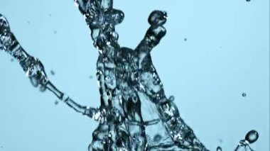 Yavaş çekim kristal berrak su sıçrayan ve havada dönen hijyen veya doğa konsepti için parlak mavi bir arka plan karşı