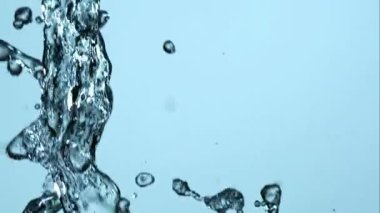 Güçlü su damlacıkları yukarı doğru fışkırarak temiz mavi zemine karşı soyut hareketlilik yaratır.