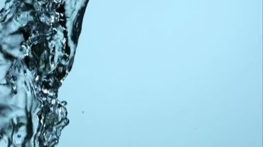 Yüksek hızlı bir kristal berrak su görüntüsü serinletici ve temiz bir doğa konsepti için açık mavi bir arka plana doğru sıçrıyor ve havada dönüyor.