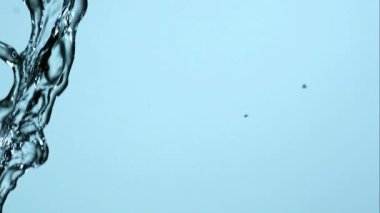 Kristal berraklığında su, açık mavi bir zemine çarpıyor ve havada dönüyor. Doğa için ferahlatıcı ve temiz sıvı hareket grafikleri oluşturuyor.