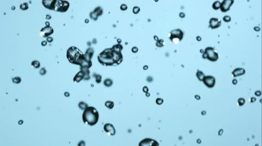 Kristal berrak su damlacıklarının ve hava kabarcıklarının makro görüntüsü yenilenen ve saf kavramlar için yumuşak mavi bir gradyan zemine karşı havadan düşüyor.