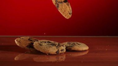 Lezzetli yuvarlak çikolatalı kurabiyeler düşüyor ve parlak ahşap bir yüzeye yığılıyor. Profesyonel bir yavaş çekim stüdyosundaki canlı kırmızı arka plana karşı.