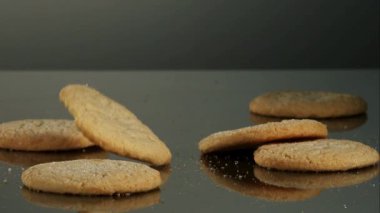 Fırın ürünü reklamları ve tatlı abur cubur pazarlama kavramları için yavaş çekimde koyu renkli bir yansıtıcı yüzeyde düşüp zıplayan altın şekerli kurabiyeler.