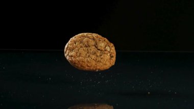 Tek bir yuvarlak yulaflı kuru üzümlü kurabiye fırın ve sağlıklı abur cubur reklamı için yavaş çekimde karanlık bir yansıtıcı yüzeye düşüp zıplıyor.