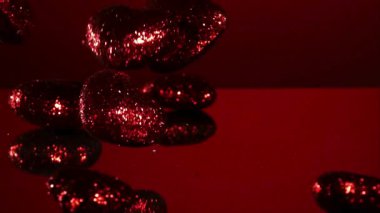 Kırmızı parıltılı kalp, sevgililer günü ve romantik aşk kutlamaları için kırmızı yansıtıcı bir ayna yüzeyinde yavaş çekimde düşerek zıplar.