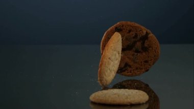 Çeşitli yuvarlak kurabiyeler ve çikolatalı bisküviler koyu mavi bir gradyan stüdyo arka planına karşı koyu bir yansıtıcı yüzeyde düşüp zıplıyorlar.