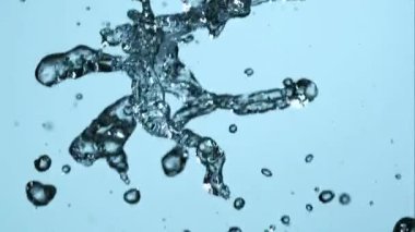 Temiz su damlacıklarının çarpıcı patlaması havada süzülürken ve hareket ederken açık mavi bir zemin üzerinde ultra yüksek hızlı ağır çekimde