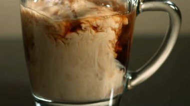 Bir bardak koyu kavrulmuş sıcak kahvenin içine dökülen sütlü ya da kremalı sinematik yakın çekim kahvaltı için yavaş çekimde güzelce karıştırılıyor.