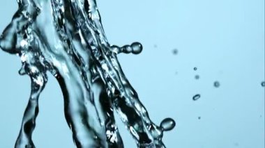 Stüdyoda parlak mavi bir zemine çarpan ve dans eden kristal berrak suyun yüksek hızda yavaş çekim videosu güzel sıvı şekiller ve desenler yaratıyor.