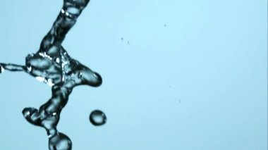 Saf kristal berrak su akıntısı yavaş çekimde yumuşak mavi bir zemine çarpıyor. Stüdyoda sıvı hareketleri ve güzel soyut su şekillerini gösteriyor.