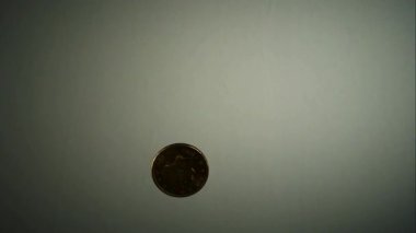 Tek bir bakır bozuk para havada sallanıyor ve ağır çekimde dönüyor. Tarafsız gri bir arkaplan, mali şansı ve karar verme mekanizmasını temsil ediyor.