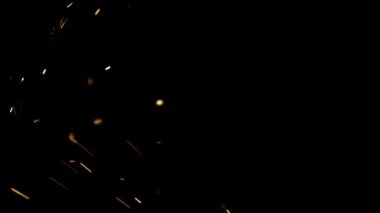 Parlak turuncu kıvılcımlar ve parlayan közler havada uçuşuyor ve karanlık atölyede bir yangın veya endüstriyel süreç sırasında siyah bir zemine doğru düşüyorlar.