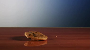 Yumuşak mavi ve beyaz stüdyo gradyan arka planına sahip koyu ahşap bir masa yüzeyine düşen ve istiflenen lezzetli çıtır çikolatalı kurabiyeler.