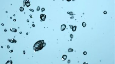 Kristal berrak su damlacıklarının soyut makro görüntüsü açık mavi arkaplana doğru yavaşça düşerek ferahlatıcı ve sakin bir atmosfer yaratıyor.