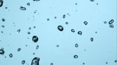 Sayısız küçük kristal berrak su damlacıkları, doğal yağmuru veya taze spreyi tasvir eden yumuşak mavi bir zemine düşüp etrafa saçılırlar.