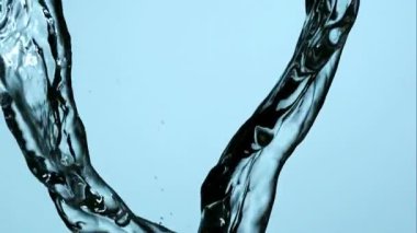 İki kalın temiz su akıntısı aşağıya doğru akıyor ve ağır çekim makro çekiminde açık mavi bir zemin üzerinde birleşiyor.