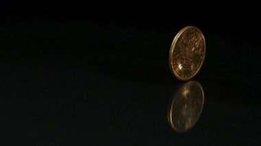 Antika altın Amerikan parası, siyah bir arkaplanda durana kadar dönen ve titreyen koyu renkli bir yüzey üzerinde sallanıyor.