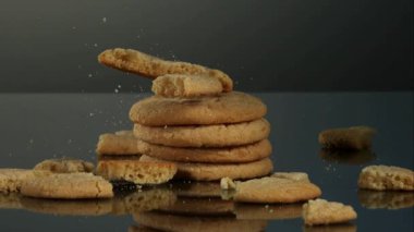 Yuvarlak şekerli kurabiye yığını, üstüne bir kurabiye düşüyor ve kırıntılar yavaş çekimde dağılıyor.