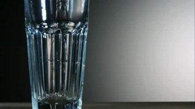 Yavaş çekimde uzun bir bardağa dökülen şeffaf sıvı, koyu ve açık gri renkli yaşam tarzı kavramlarına karşı ahşap bir tabloda.