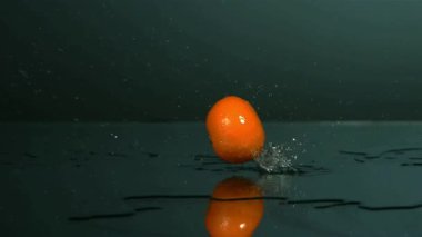 Taze bir portakal meyvesi ıslak, karanlık bir yüzeye yavaşça düşüyor. Su sıçrıyor ve damlacıklar yeni bir konsept için uçuyor.