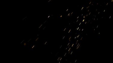 Parlak altın kıvılcımlar ve parlayan parçacıklar sinematik görsel efektler için ağır çekimde katı siyah bir arkaplan üzerinde havada uçuyor.