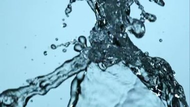 Kristal berrak su, açık mavi bir zemine karşı yavaş çekimde sıçrıyor ve akıyor. Serinletici görüntüler için güzel sıvı şekiller ve damlacıklar yaratıyor.