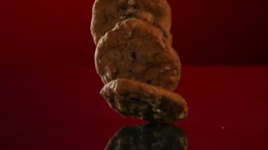 Fırında pişmiş çikolatalı kurabiyeler yavaş çekim stüdyosundaki koyu kırmızı yansıtıcı yüzeyde üstüste düşüyor ve üst üste yığılıyorlar.