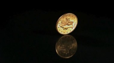 Karanlık bir yansıtıcı yüzeyde hızla dönen antik altın sikke siyah arka planda güzel bir ayna efektiyle metalin ince detaylarını gösteriyor.