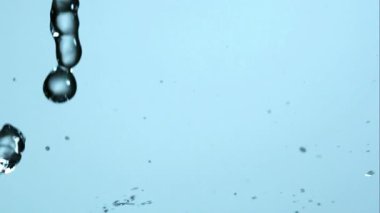 Doğa ve saflık temaları için yavaş çekim yüksek hız videosunda yumuşak mavi bir arkaplan üzerinde akan ve su sıçrayan temiz su akıntıları