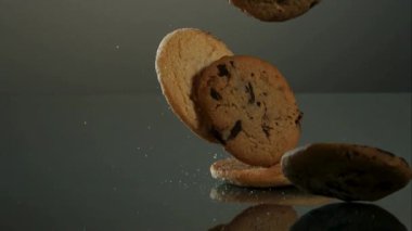 Stüdyoda uçuşan şeker kırıntılarıyla birlikte yavaş çekimde yansıtıcı karanlık bir yüzeye düşen lezzetli kurabiyeler ve bisküvilerin karışımı.