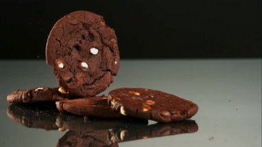 Beyaz çikolata parçalı siyah çikolatalı kurabiyeler yavaş çekimde yansıtıcı bir ayna yüzeyinde zıplıyorlar.