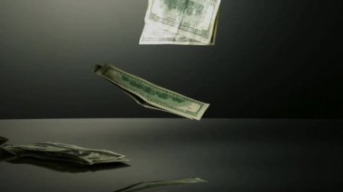 100 dolarlık banknotlar bugün servetini ve finansal başarısını temsil eden stüdyo aydınlatmasının altında karanlık bir yansıtıcı yüzeye düşüyor ve iniyor.