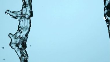 Kristal berrak su akıntıları dikey olarak soluk mavi bir zemin üzerine düşüyor ve su damlacıkları ve kabarcıkları yüksek hızda yakalanıyor.