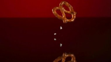 Çıtır çıtır tuzlu krakerler düşüyor ve yansıtıcı kırmızı bir yüzeye zıplıyor yavaş çekimde tuz taneleri etrafa saçılıyor.