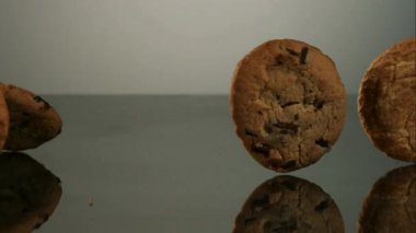 Çeşitli yeni pişmiş gurme kurabiyeler, temiz beyaz stüdyo arka planına karşı yavaş çekimde koyu gri bir yüzey boyunca yuvarlanıyor.