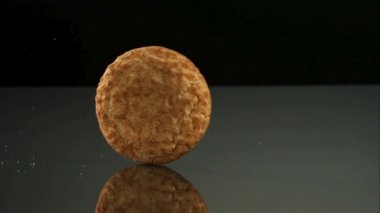 İki farklı yuvarlak kurabiye türü koyu bir yansıtıcı yüzeyde yuvarlanıyor ve çerçeveden koyu siyah bir zemine doğru kayboluyor.