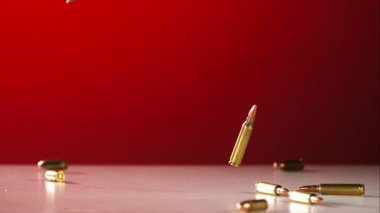 Pirinç tüfekli mermiler, beyaz bir zeminde ağır çekimde, ağır çekimde mermi kovanlarıyla çarpıcı bir kırmızı zemine çarpıp zıplıyorlar.