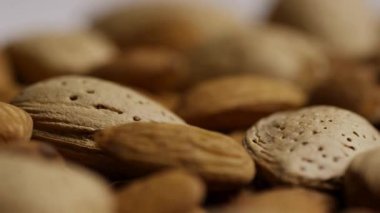 Büyük bir ham organik badem koleksiyonu. Kabuklarında ve kabuklarında yumuşak doğal ışık altında bir masada yan yana yatıyorlar.