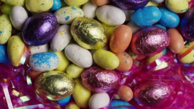Çok renkli paskalya yumurtaları ve çikolata şekerlerinin üst görüntüsü. Bayram kutlaması ve şenlikli dekorasyon konsepti için parlak pembe süslemelerle harmanlanmış.